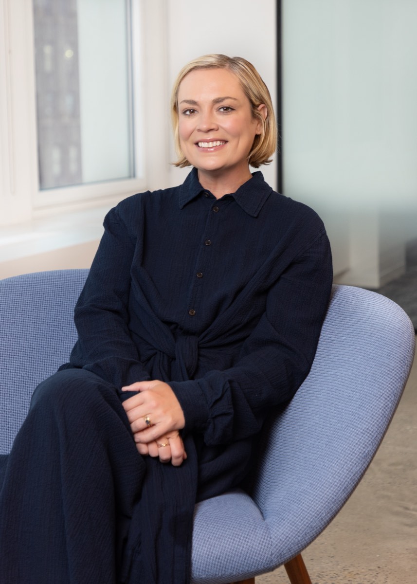Portrait of a woman with short blonde hair in navy, seated in an armchair